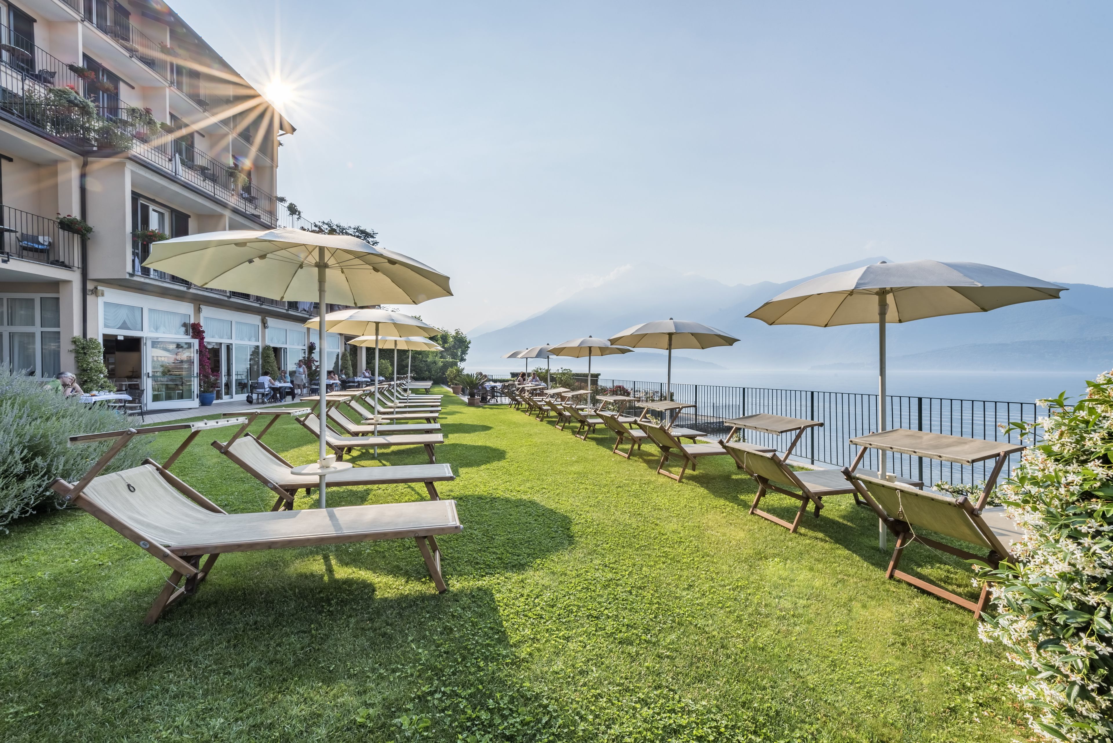 A rooftop terrace with sun loungers and umbrellas, overlooking a body of water and mountains.
