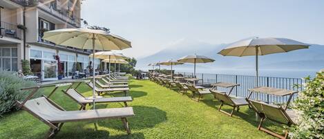 Une terrasse sur le toit, dotée de chaises longues et de parasols, offrant une vue sur un plan d’eau et des montagnes.