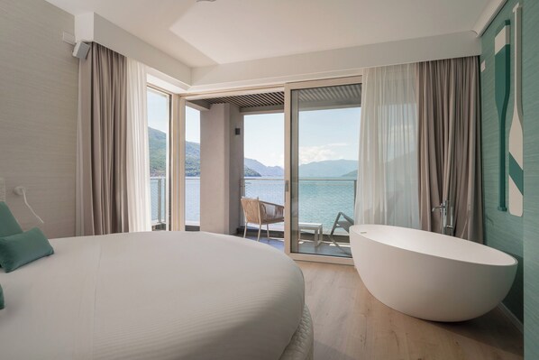 Un dormitorio con una cama grande, una bañera y un balcón con vistas al agua y las montañas.