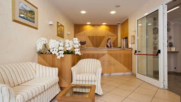 A hotel reception area with a reception desk, two striped sofas, a glass coffee table, and a wall with framed pictures and a decorative plate collection.