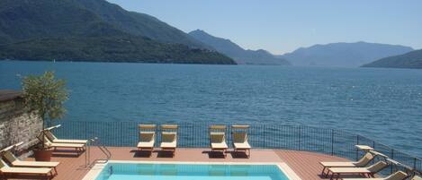 A pool area with lounge chairs and a view of a lake surrounded by mountains.