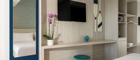 Una habitación de hotel moderna con una cama, un televisor montado en la pared, una planta pequeña y un reposapiés azul.
