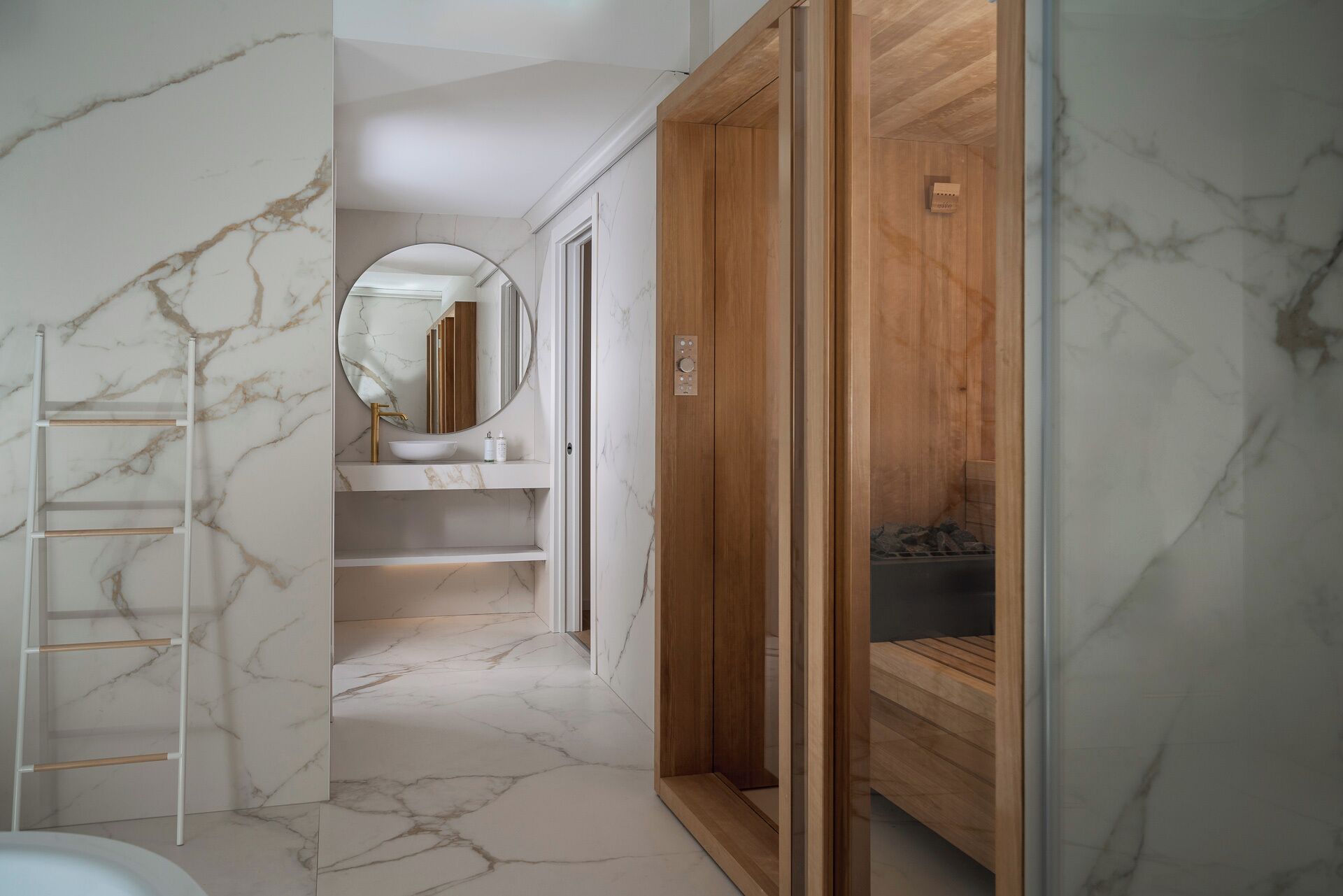 A bathroom with a marble floor, a wooden vanity, a round mirror, and a shower enclosure.