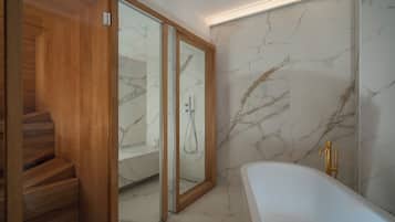 A modern bathroom with a marble wall, a freestanding bathtub, and a wooden staircase leading to a shower area.