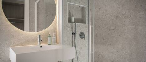 Un baño con lavamanos blanco, un espejo redondo y zona de ducha.