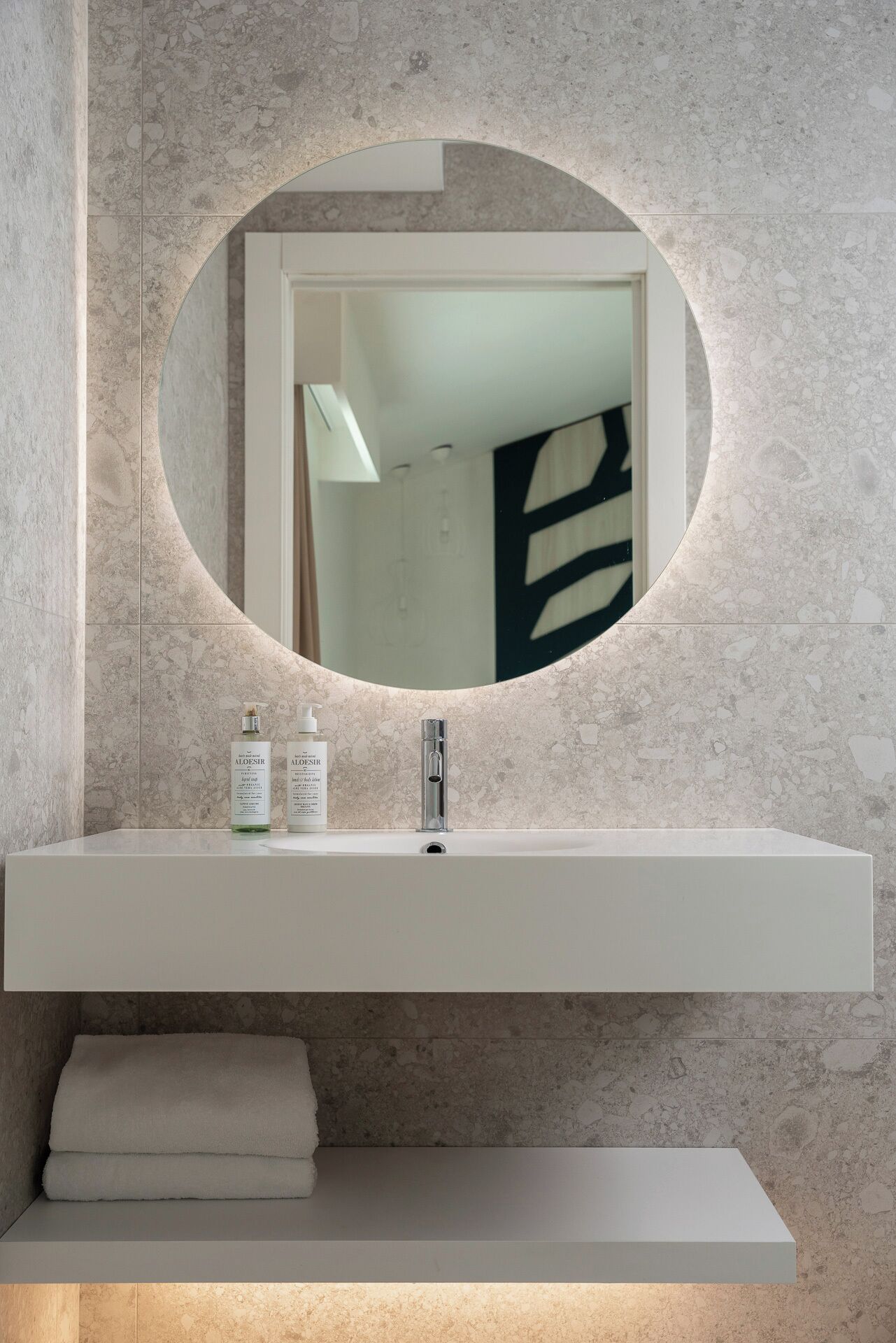 A modern bathroom with a round mirror, a white sink, and two bottles of lotion.