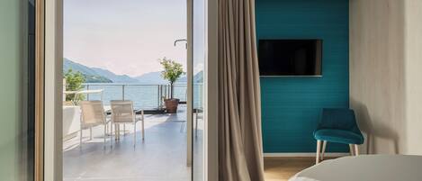 Habitación de hotel moderna con balcón con vistas a un lago y montañas.