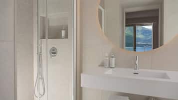 A modern bathroom with a glass-enclosed shower, a white sink with a mirror above it, and toiletries on the sink.