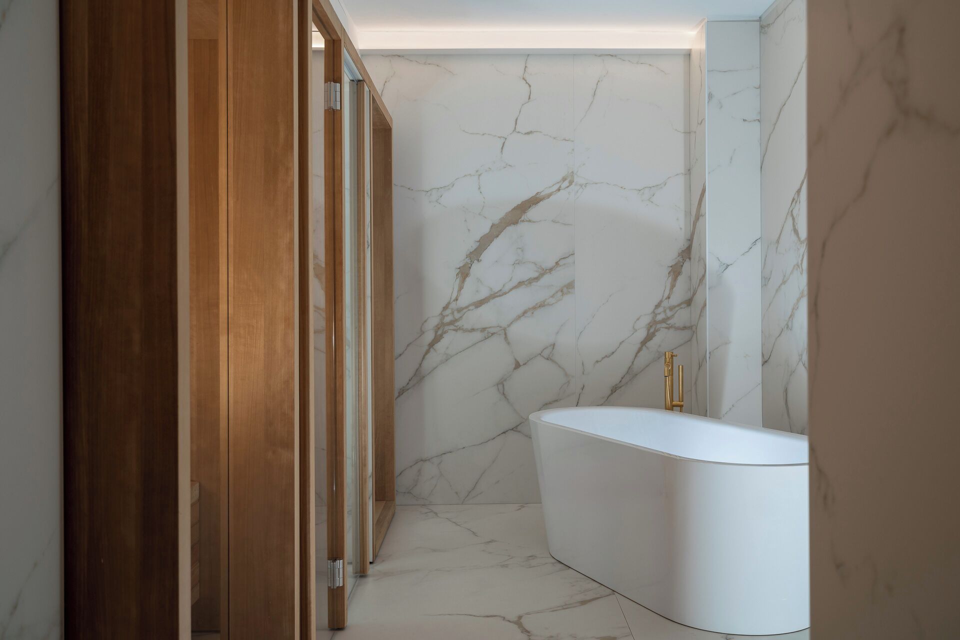 A modern bathroom with a marble wall, a wooden door, and a white bathtub.