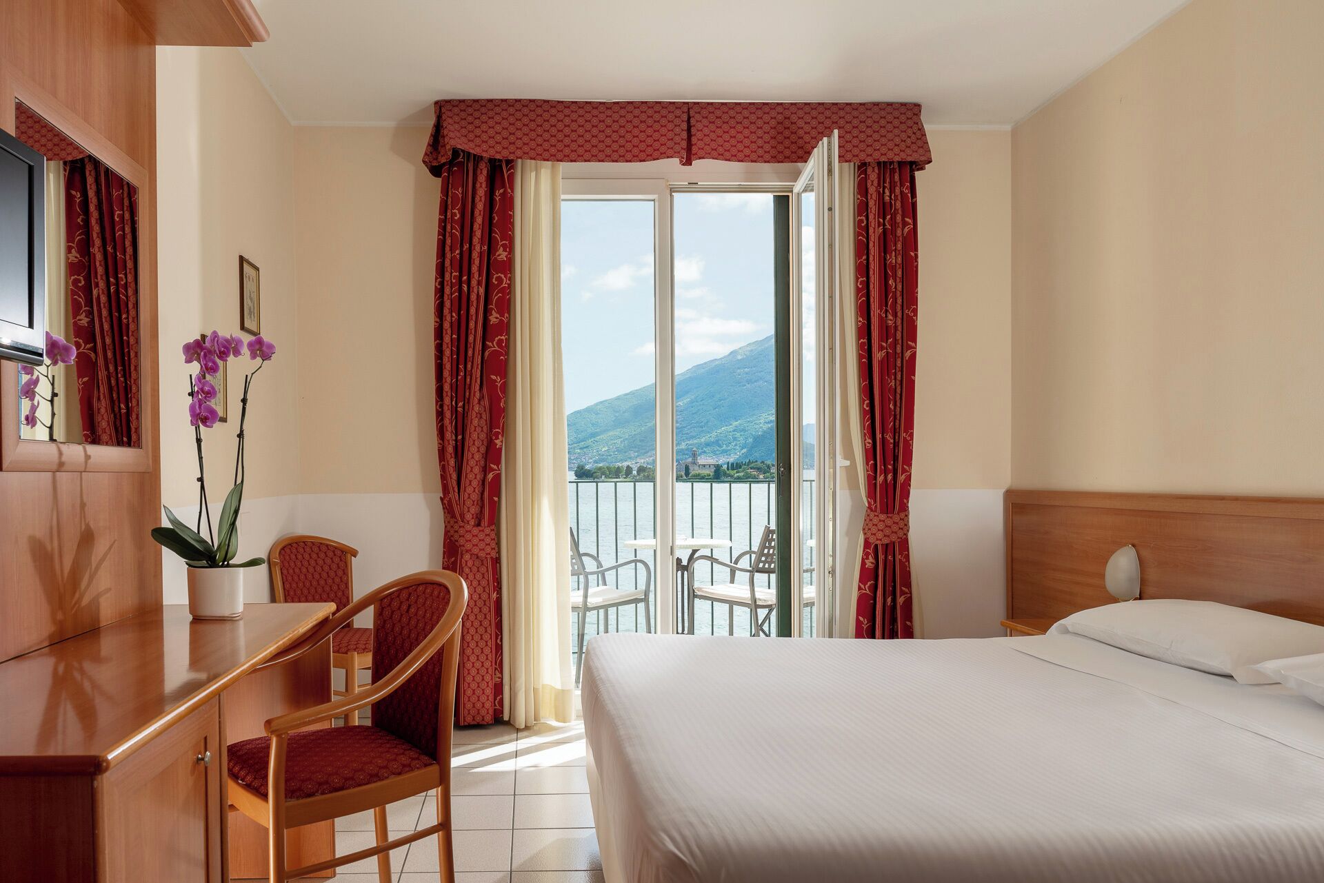 A hotel room with a bed, a desk, a chair, and a balcony with a mountain view.
