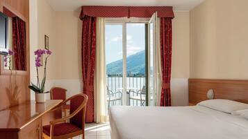 A hotel room with a bed, a desk, a chair, and a balcony with a mountain view.