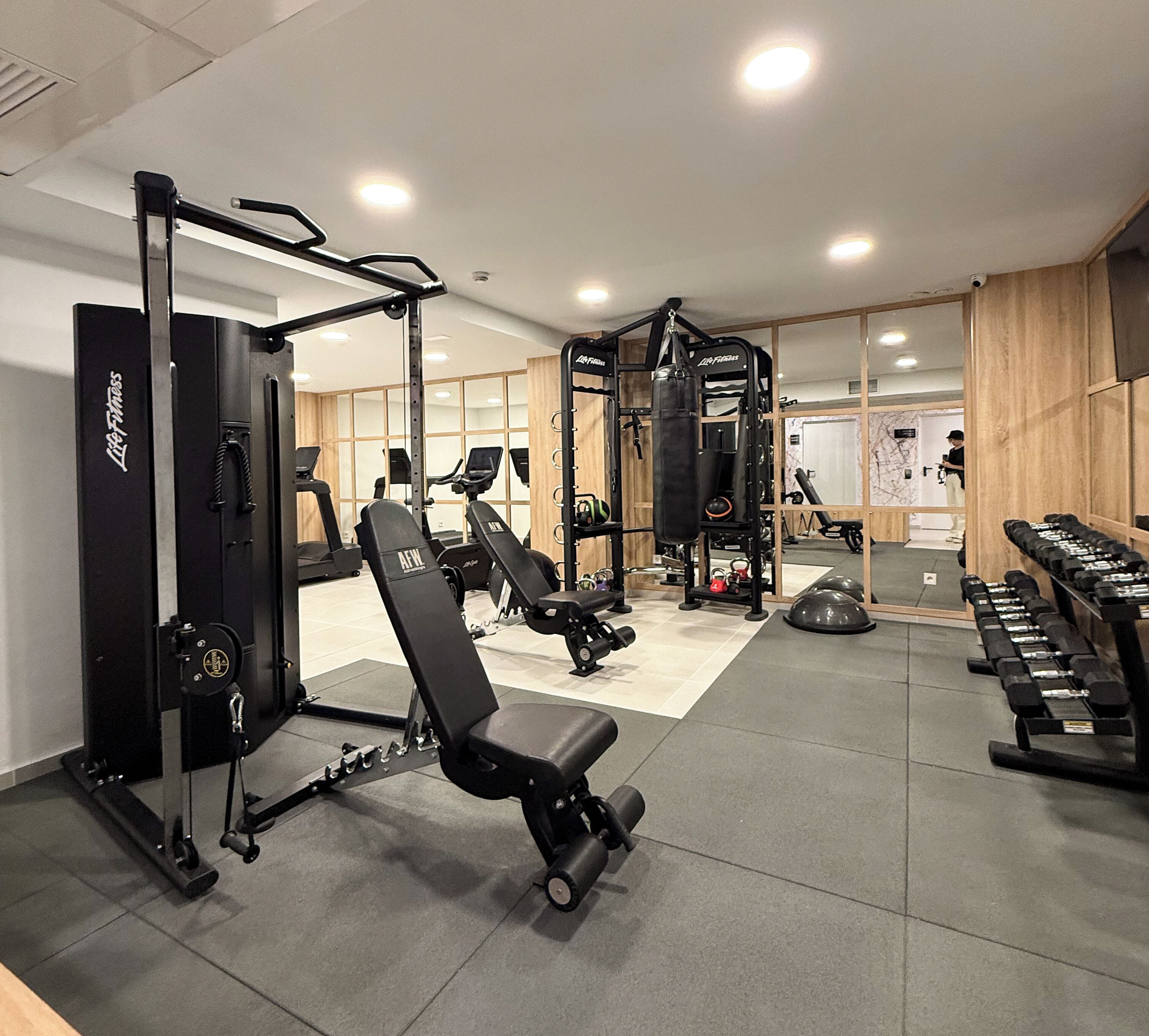 A gym with weightlifting equipment, treadmills, and a mirrored wall.