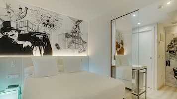 A modern hotel room with a large bed, a bedside table, and a wall with black and white artwork.