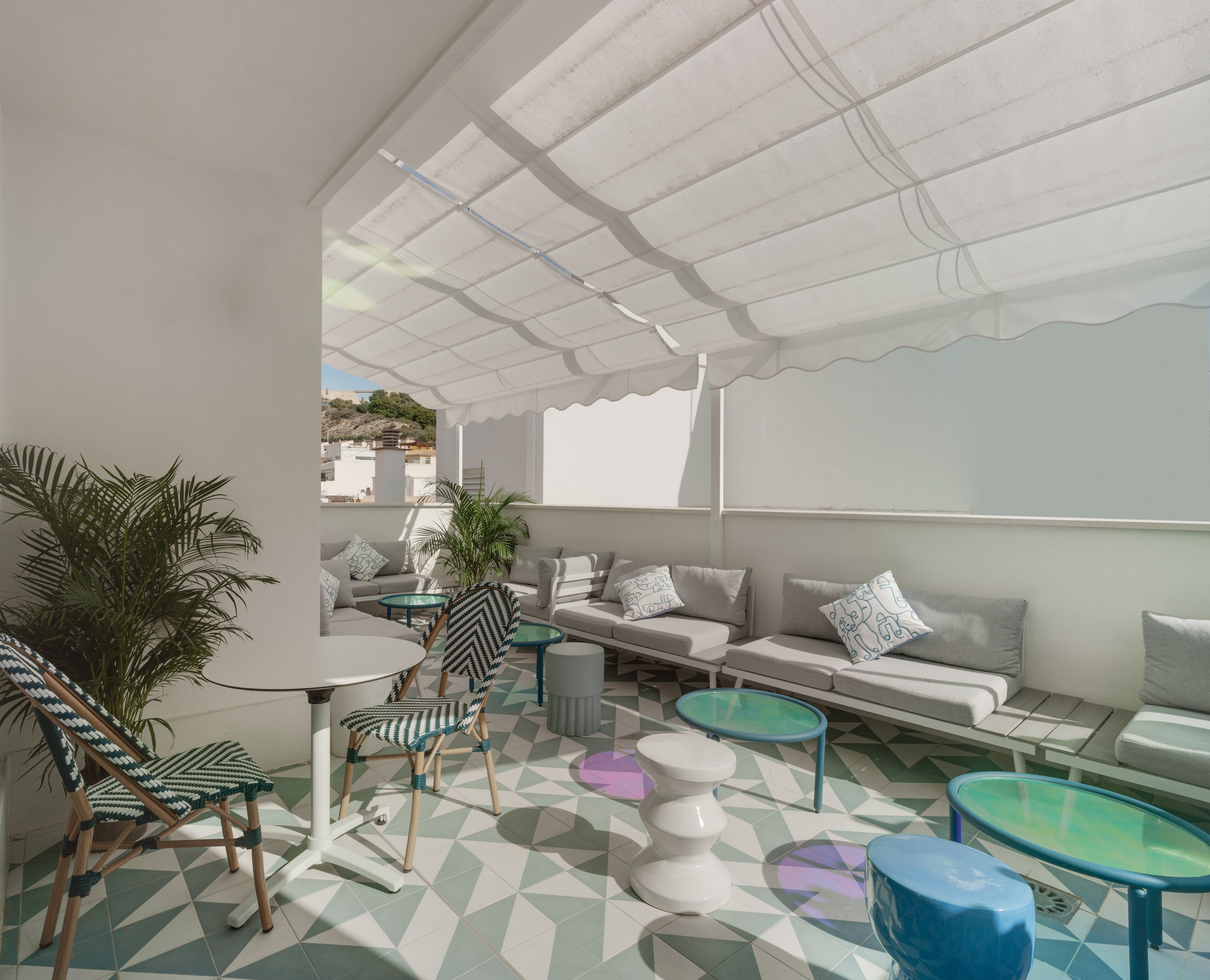 An outdoor seating area with a white ceiling, geometric patterned floor, and a variety of seating options including a sofa, chairs, and tables.