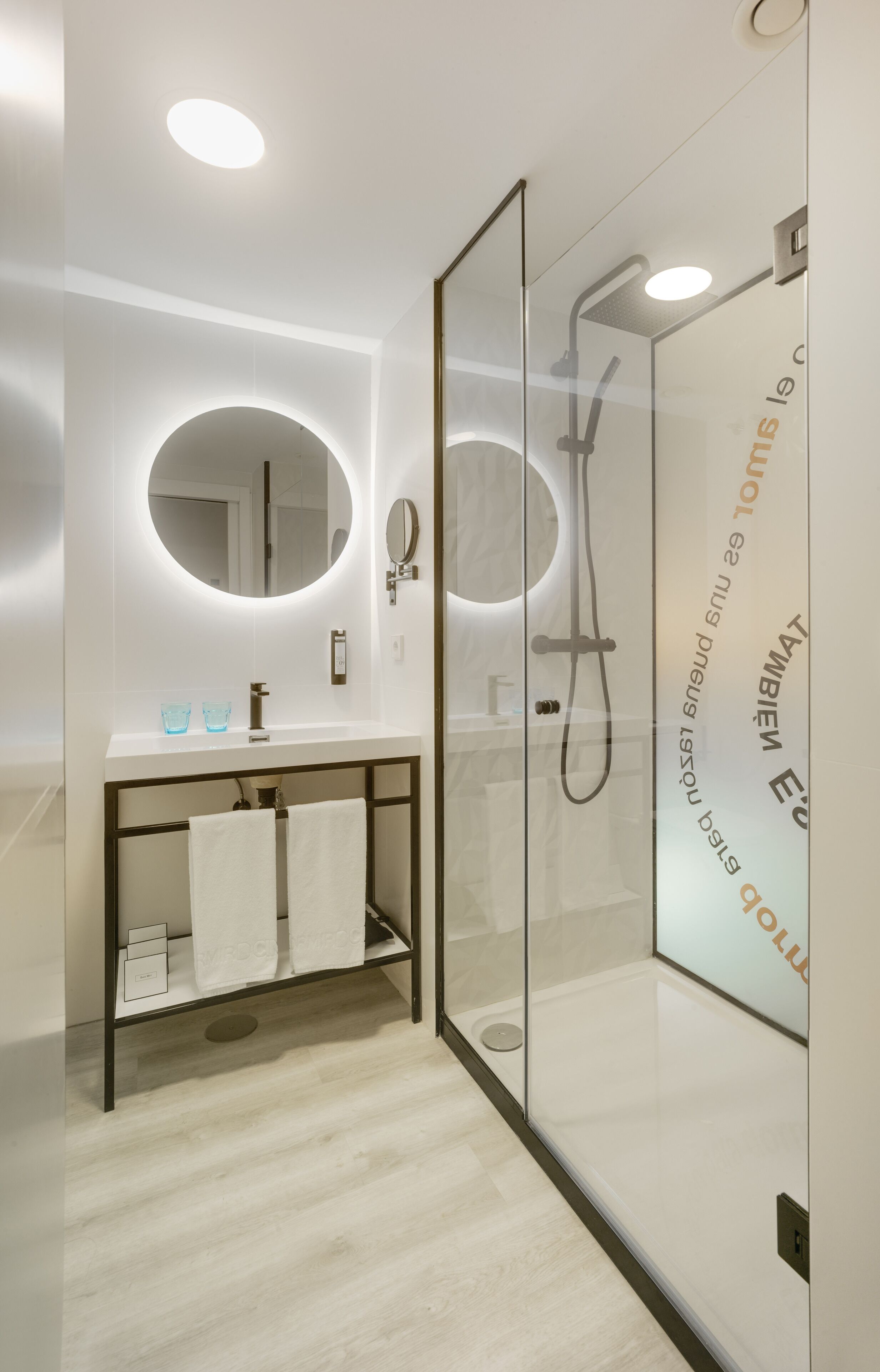 Un baño moderno con cabina de ducha de vidrio, un espejo redondo y un mueble de tocador con toallero.