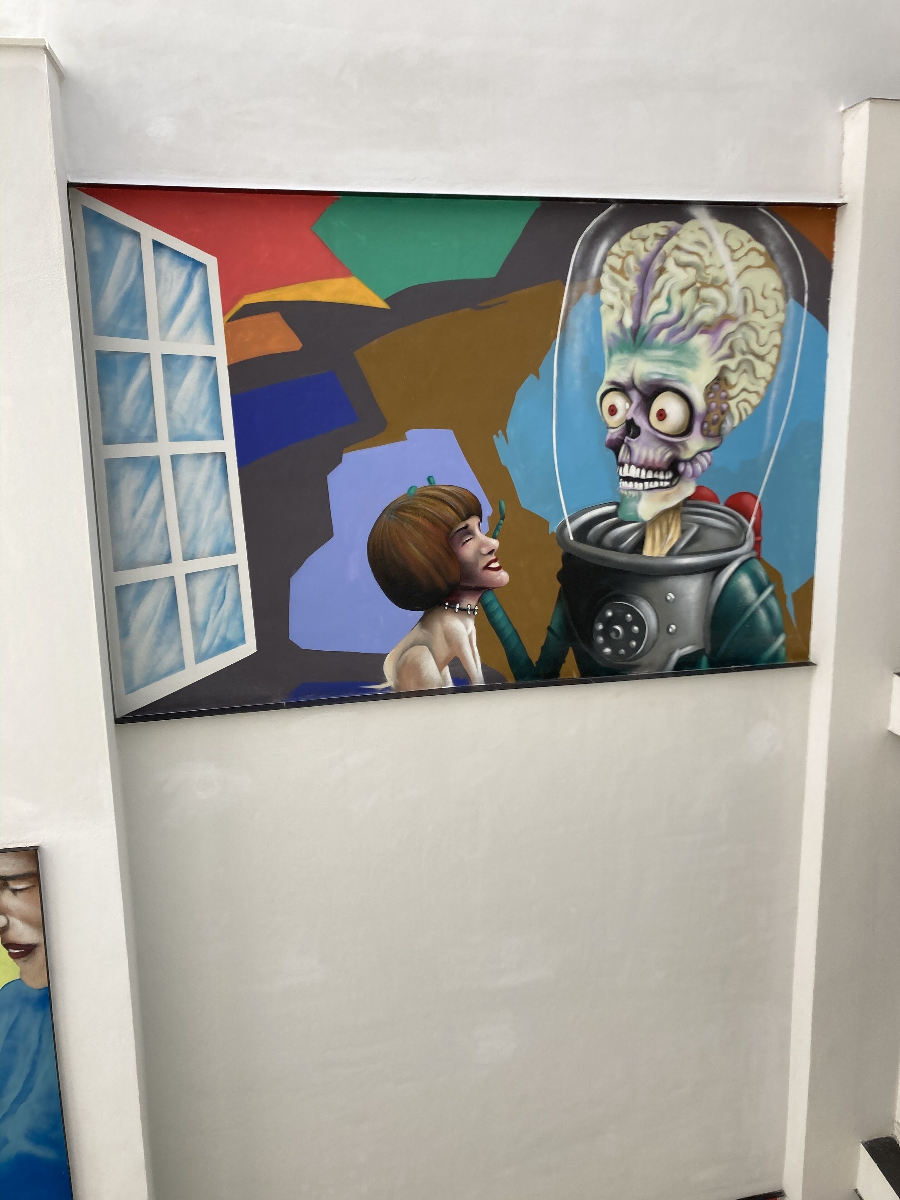 Un mur orné d’une peinture abstraite aux couleurs vives, représentant une figure et un objet ressemblant à un crâne.