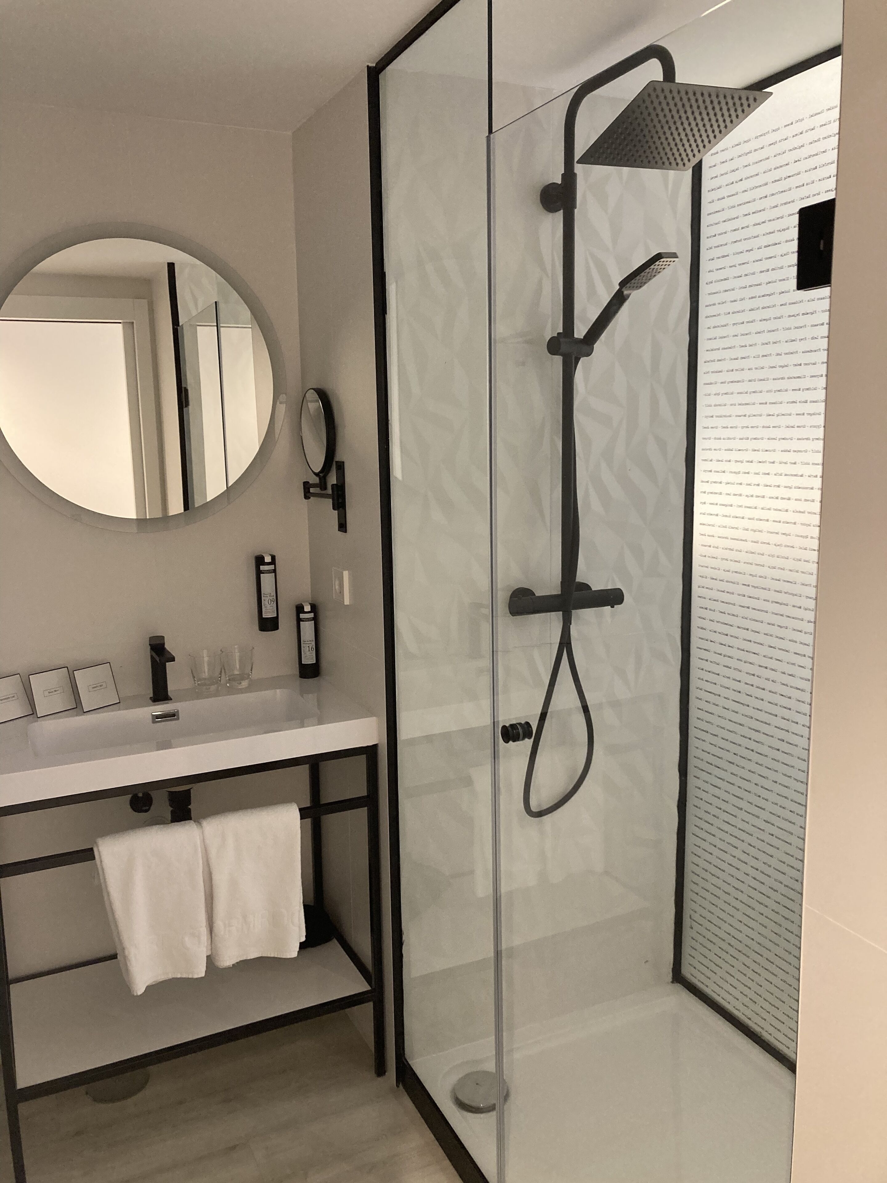 Un baño moderno con ducha de vidrio, espejo redondo, lavabo blanco y toallero.