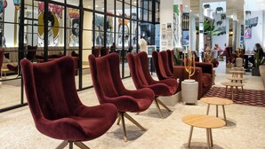 Un hall d’entrée spacieux, doté de chaises rouges modernes, de tables en bois et d’un sol carrelé.