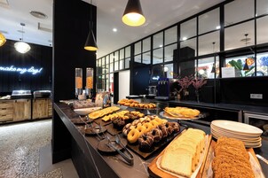A buffet with various food items, including pastries and bread, in a modern kitchen setting with black countertops and pendant lighting.