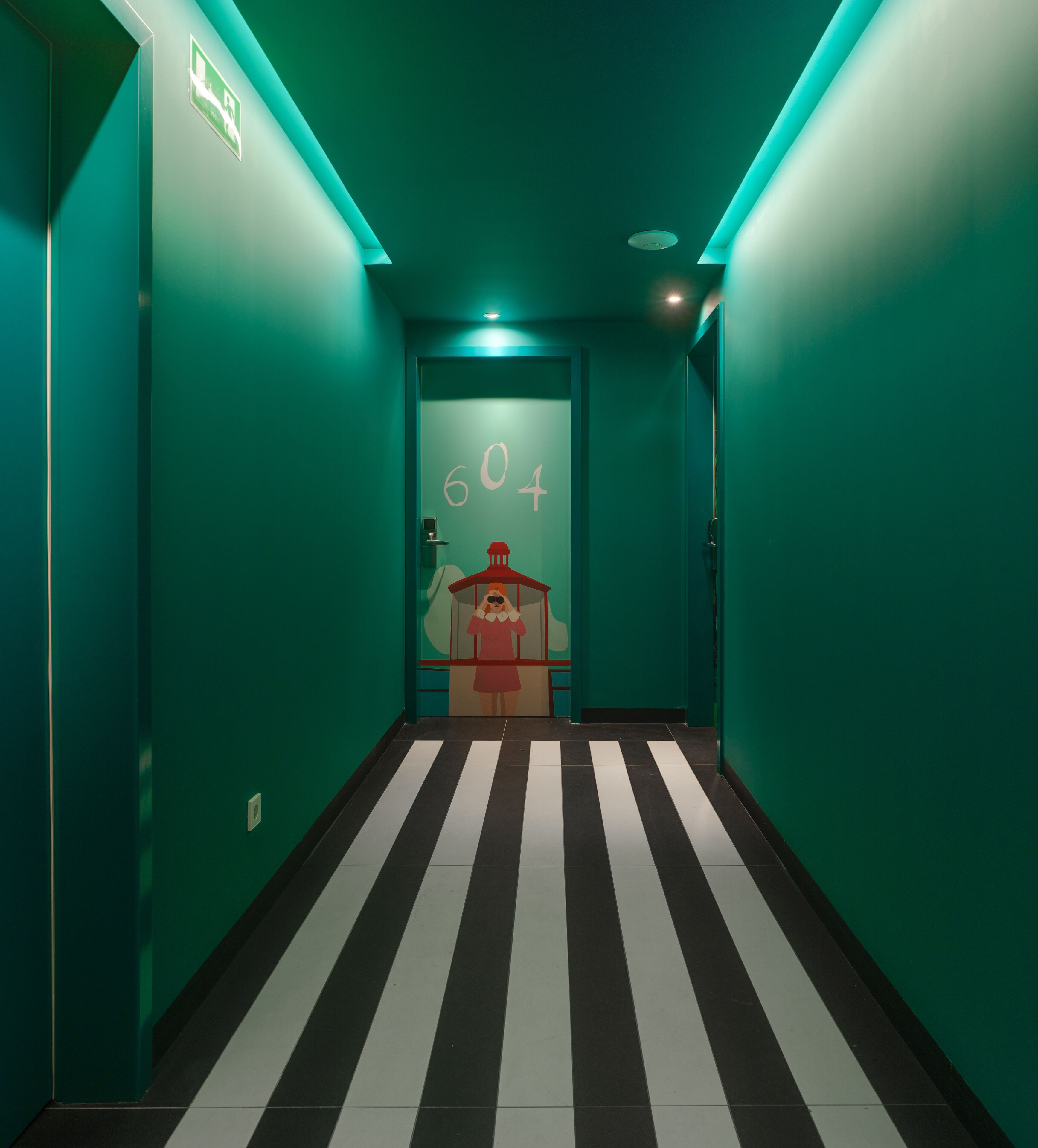 A hallway with teal walls, a black and white striped floor, and a door marked with the number 604.