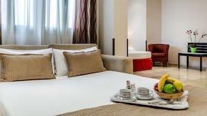 A hotel room with a bed, a dining table with a fruit basket, and a red chair. - Hotel Exe Suites 33 (Madrid)