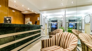 A reception area with a wooden reception desk, a glass wall, and striped chairs. - Hotel Exe Suites 33 (Madrid)