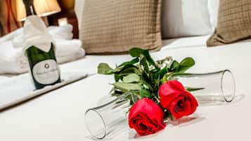 Una cama con un ramo de rosas rojas en un florero de vidrio, una botella de champán y una almohada a cuadros.