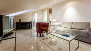 A modern living room with a glass coffee table, a red armchair, a grey sofa, and a television. - Hotel Exe Suites 33 (Madrid)