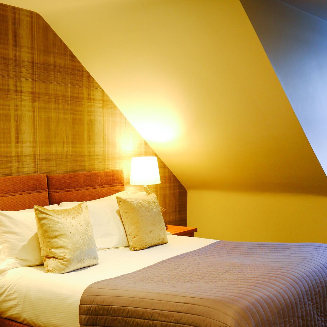 Een slaapkamer met een schuine plafond, een bed met wit en bruin beddengoed, en een bedlampje.