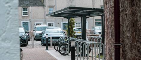 A parking area with bicycles, cars, and a building in the background.
