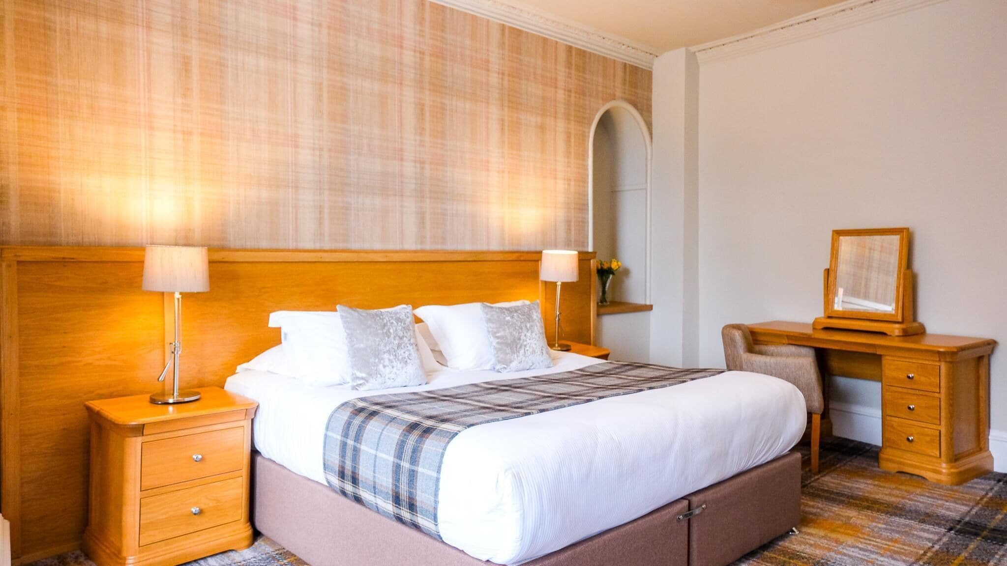 A hotel room with a large bed, two bedside tables, a desk with a chair, and a mirror.