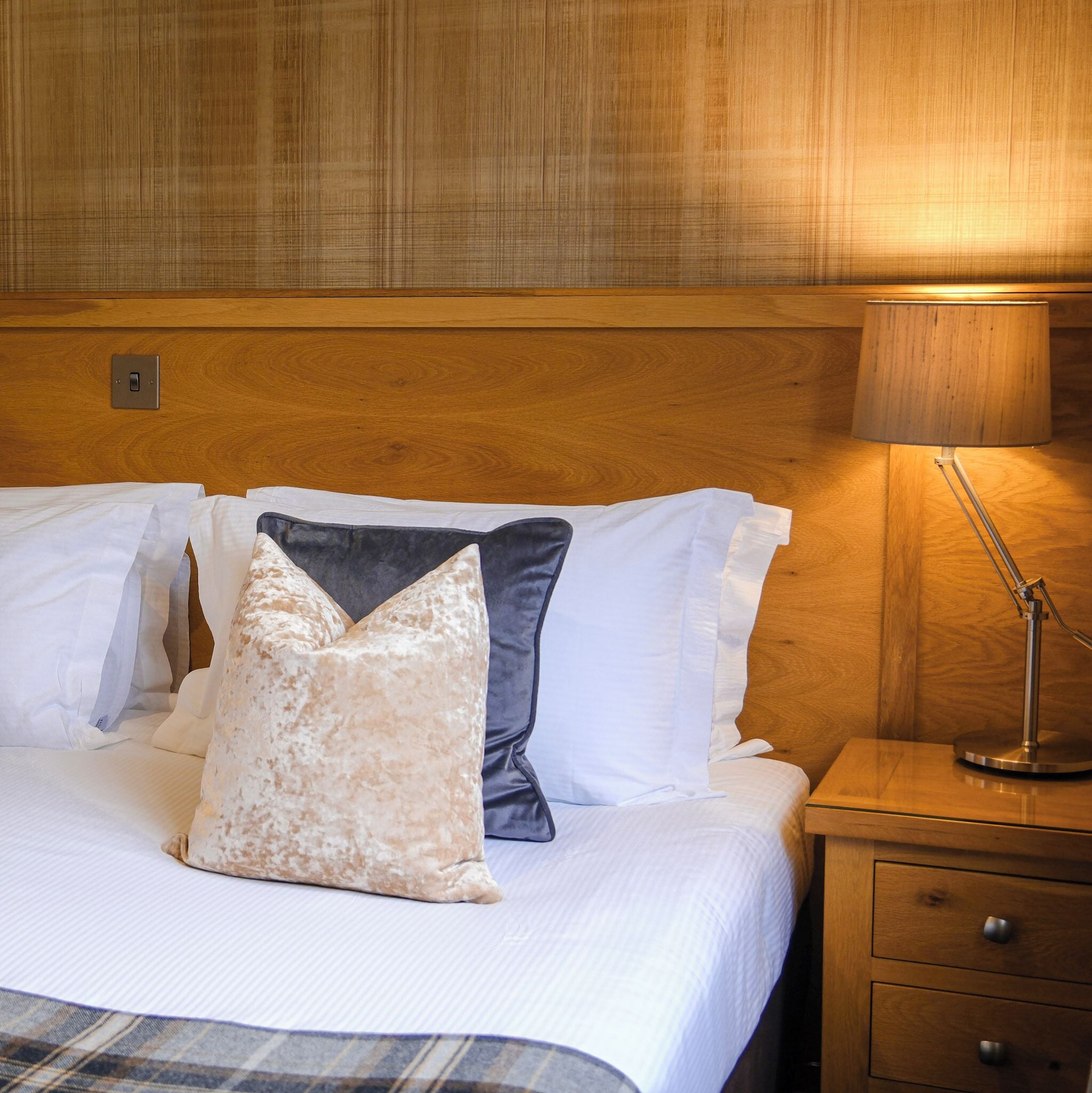 A neatly made bed with white and grey linens, a wooden headboard, and a bedside table with a lamp.