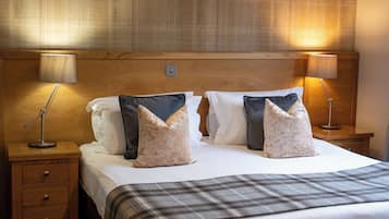 A neatly made bed with a plaid bedspread, two bedside lamps, and a wooden headboard.