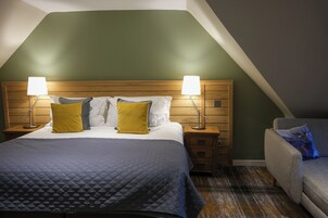 Habitación de hotel con una cama grande, dos mesitas de noche con lámparas, un cabecero de madera y una pared verde decorativa.