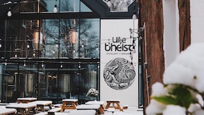 A distillery with a large sign reading "like theist" and outdoor seating with benches covered in snow.