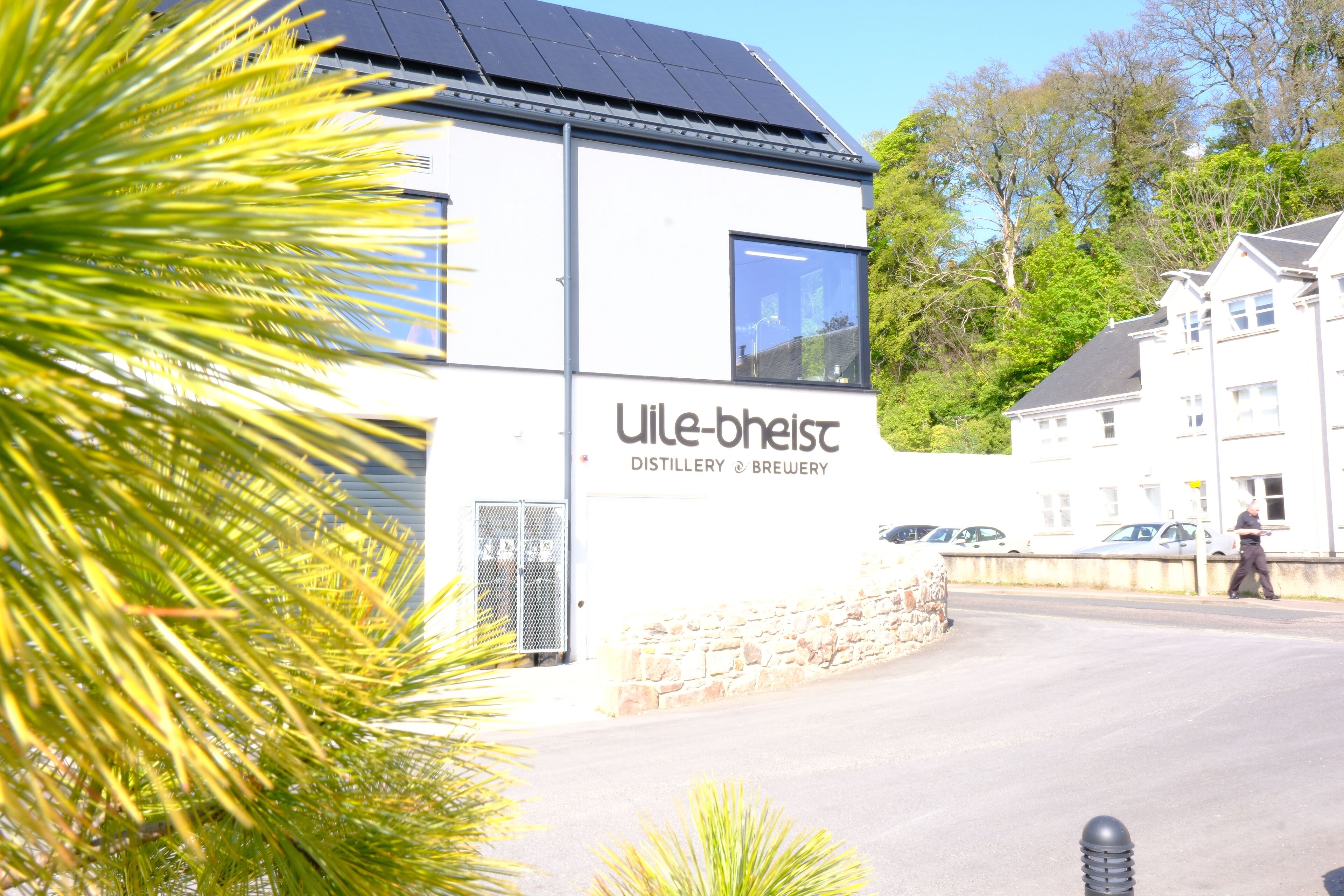 Un bâtiment sur lequel on peut lire l’inscription « Uile-bheist Distillery & Brewery », avec un mur de pierre devant.