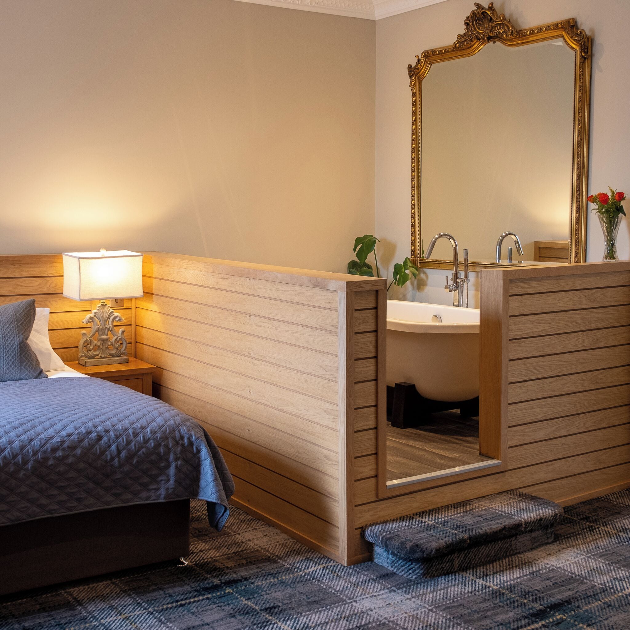 Une chambre d’hôtel avec un lit, une lampe de chevet, un lambris en bois, un lavabo et un miroir.
