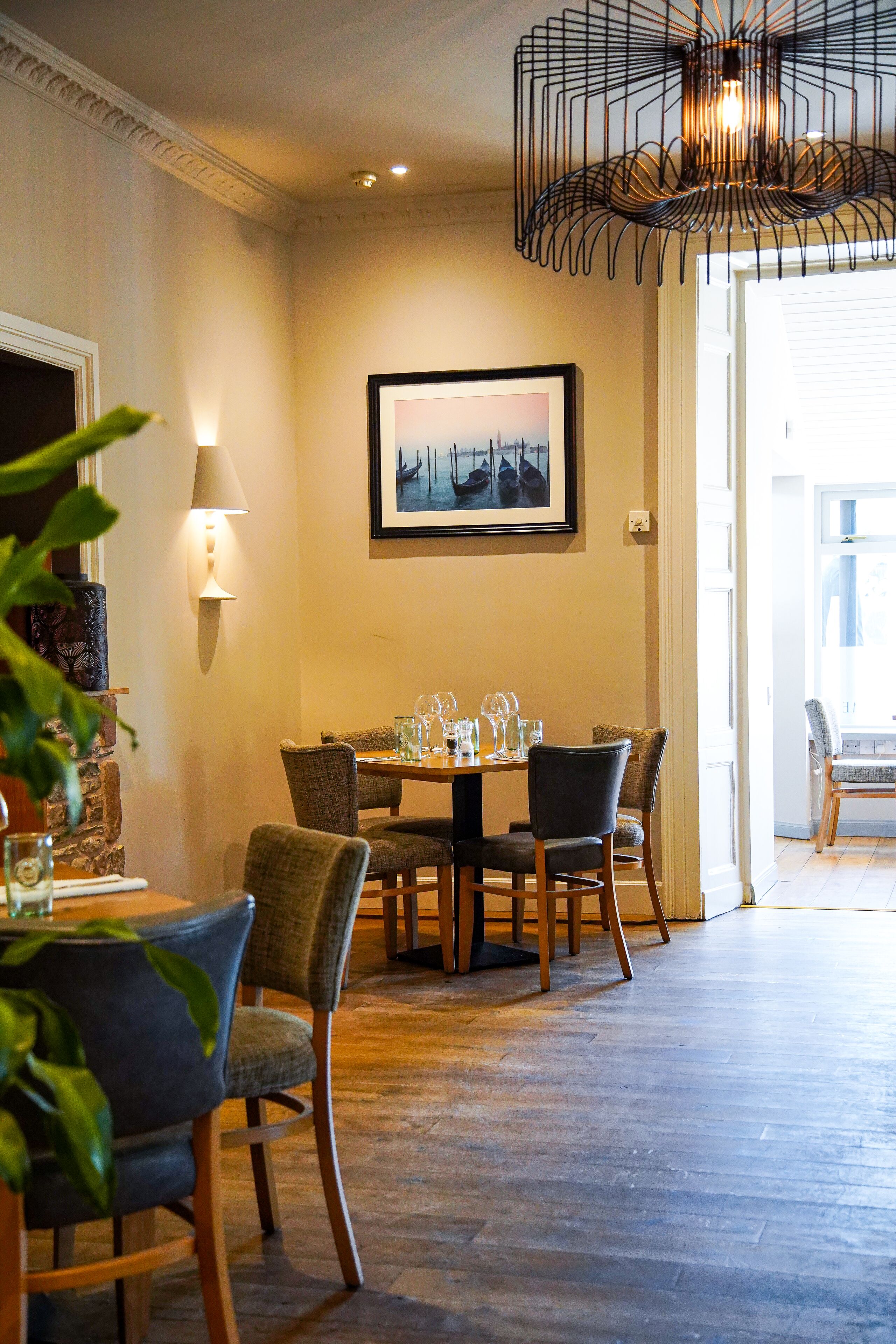 A dining area with a table set for four, surrounded by chairs, a framed picture on the wall, and a modern pendant light.