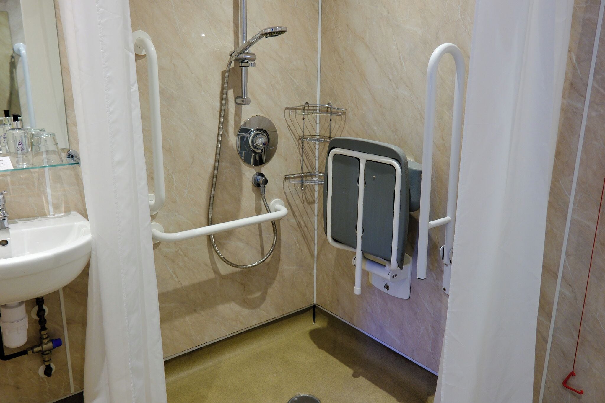 A bathroom with a sink, a shower with a handheld showerhead, and a grab bar.