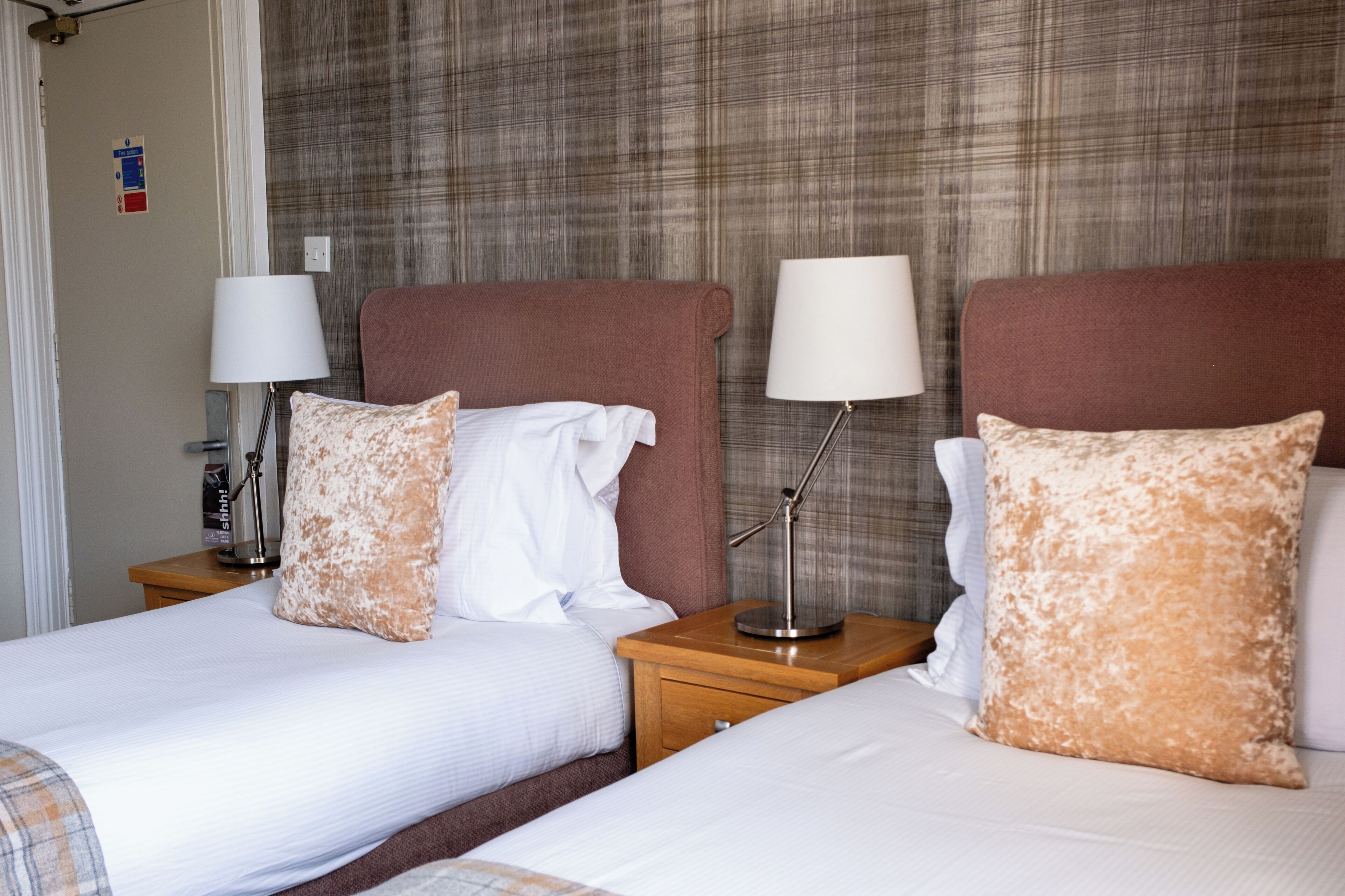 A hotel room with two beds, each with a pillow and a lamp on a wooden nightstand.