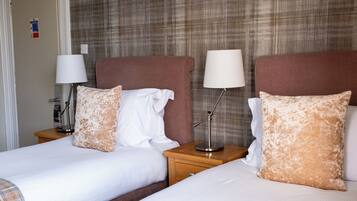 A hotel room with two beds, each with a pillow and a lamp on a wooden nightstand.