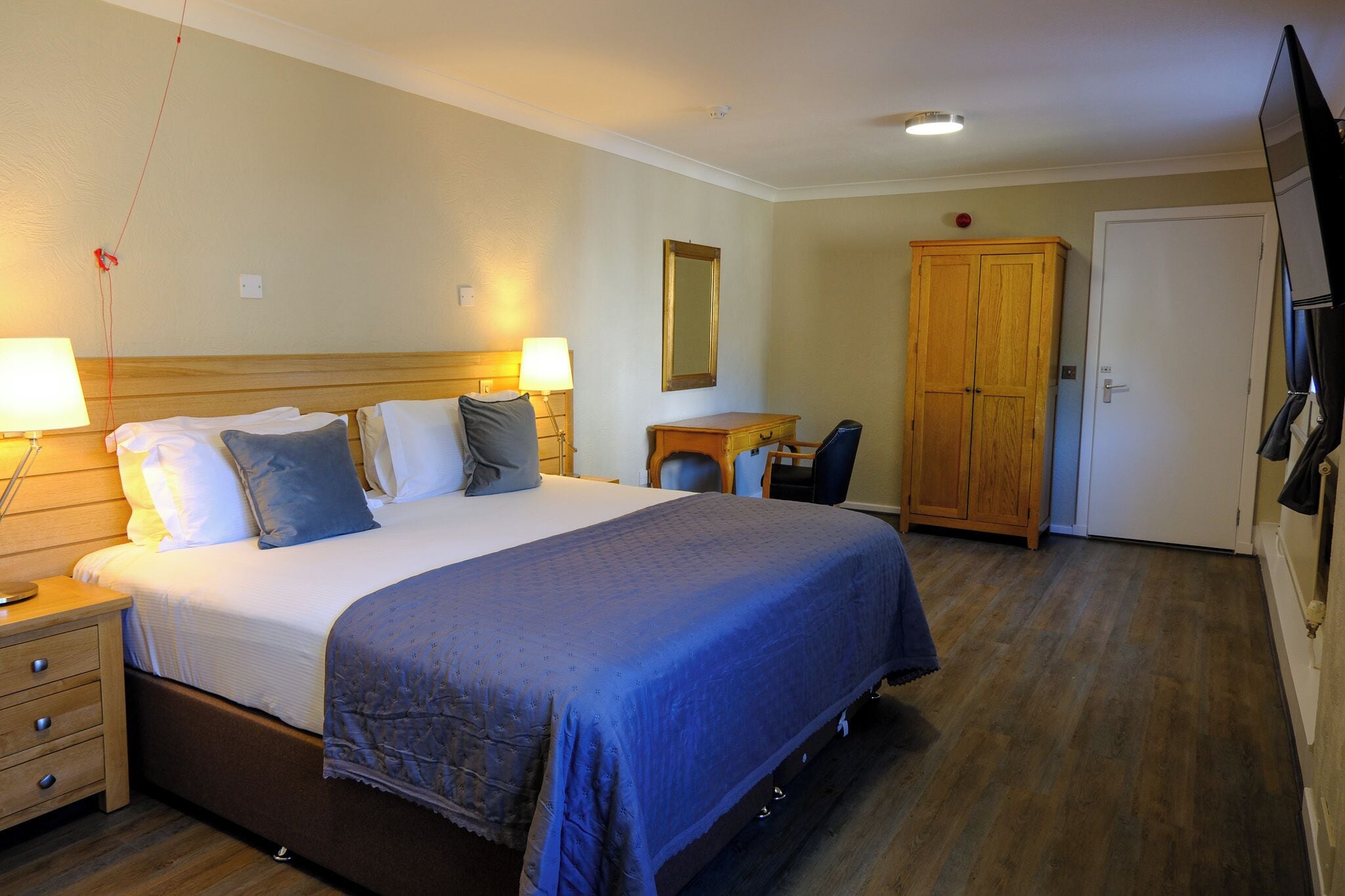 A hotel room with a bed, bedside tables, a desk, a chair, a wardrobe, and a television.
