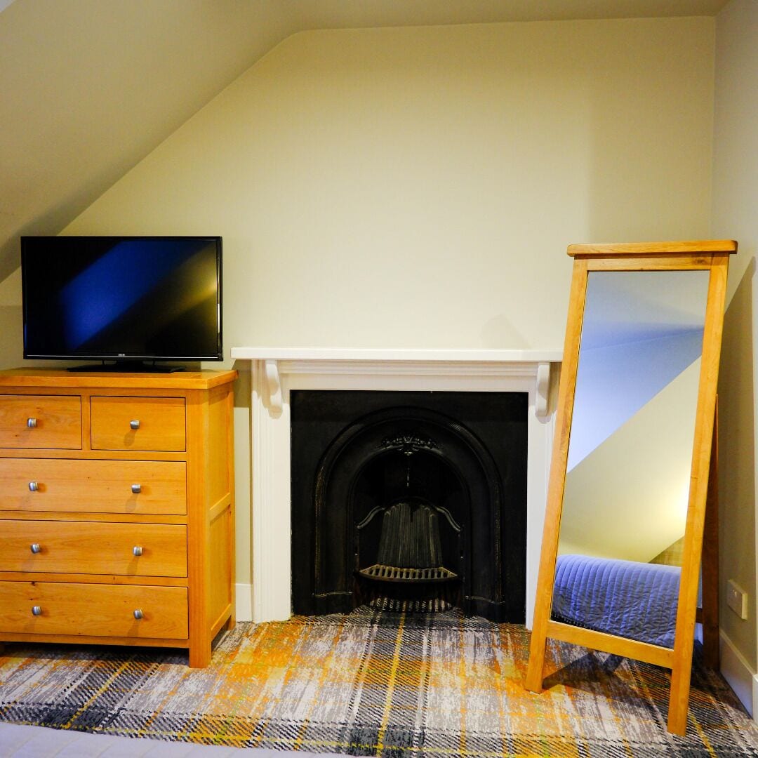 Una habitación con chimenea, un televisor sobre una cómoda de madera y un espejo apoyado en la pared.