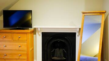 Una habitación con chimenea, un televisor sobre una cómoda de madera y un espejo apoyado en la pared.