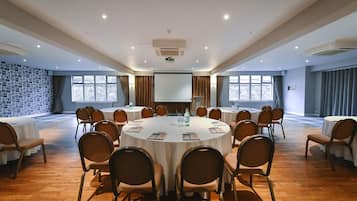 A conference room with round tables, chairs, a projector screen, and large windows.