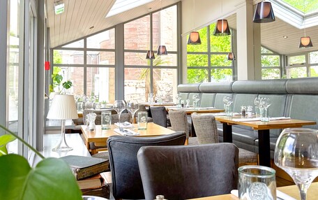 A restaurant with wooden tables, comfortable seating, and large windows allowing natural light.
