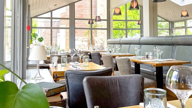 A restaurant with wooden tables, comfortable seating, and large windows allowing natural light.