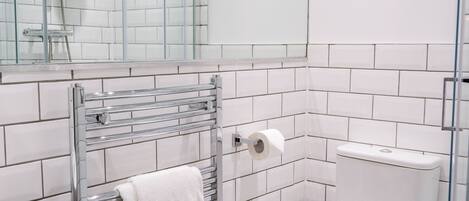 Un baño con azulejos blancos, cabina de ducha de vidrio, inodoro y toallero con una toalla blanca.