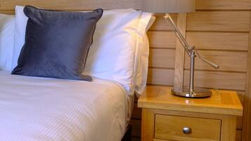 A neatly made bed with white and gray linens, a wooden headboard, and a bedside table with a lamp and drawers.