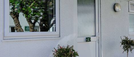 A building facade with a door marked '12', a window reflecting trees, and two potted plants.